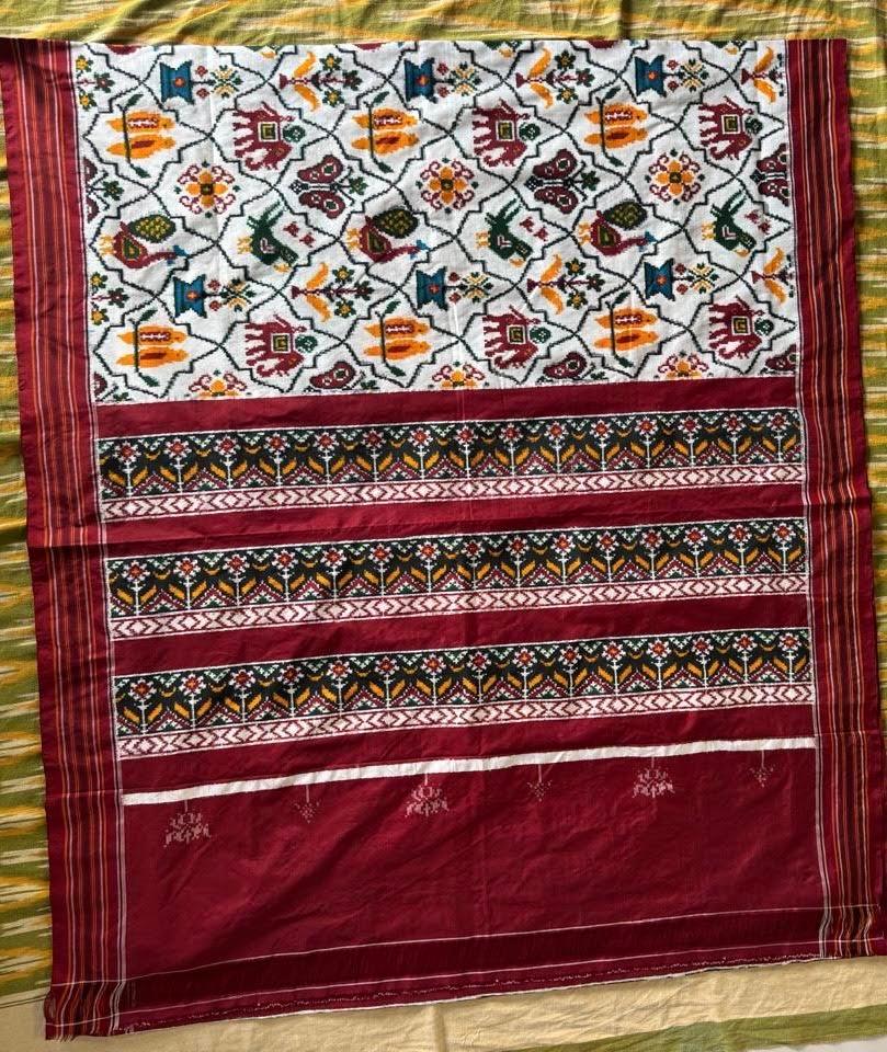 Flat lay of a traditional Patola Ikat saree with a white body featuring elephant and parrot motifs, and a contrasting rich maroon pallu.