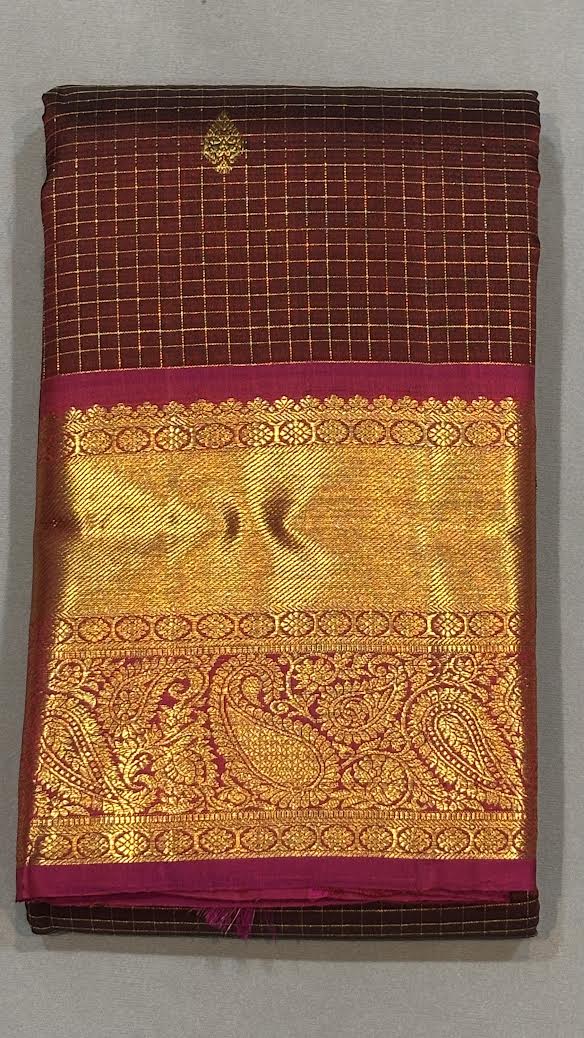 A woman seated elegantly wearing an authentic maroon Kanchipuram pattu saree featuring gold zari micro-checks and a heavy contrasting pink brocade pallu."