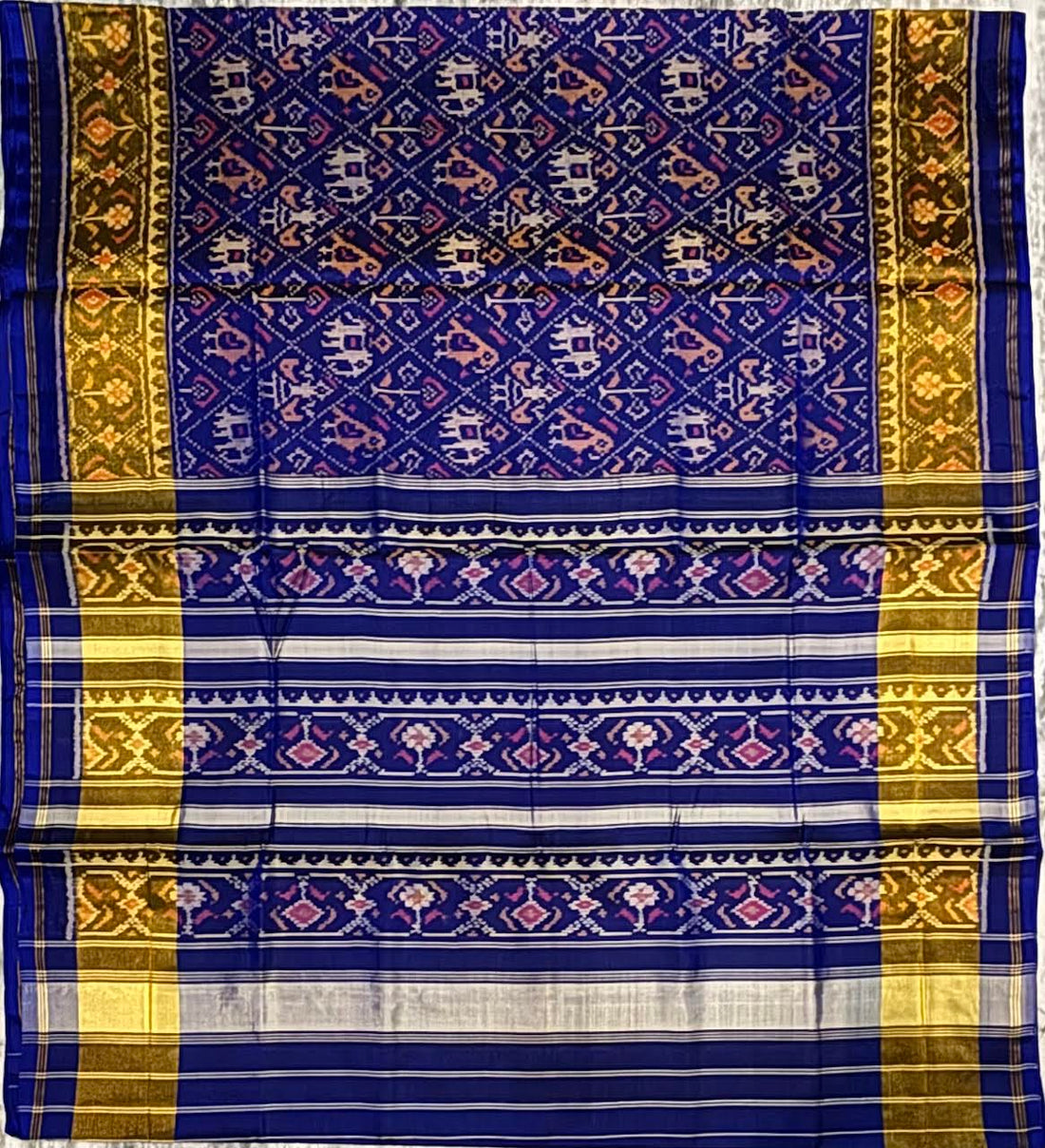 Close-up of a blue Patola silk saree pallu featuring horizontal stripes, gold zari, and traditional pink and white geometric Ikat patterns.
