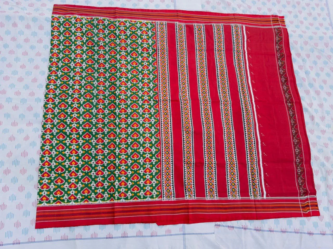 Flat lay of an authentic double ikat patola silk saree with a bold green patterned body, red striped pallu, and Silk Mark certification