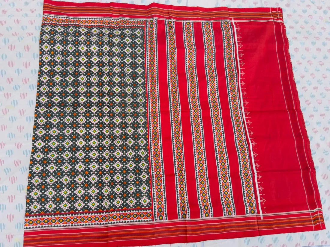 Flat lay of an authentic double ikat patola silk saree with a charcoal black geometric patterned body, red striped pallu, and Silk Mark certification