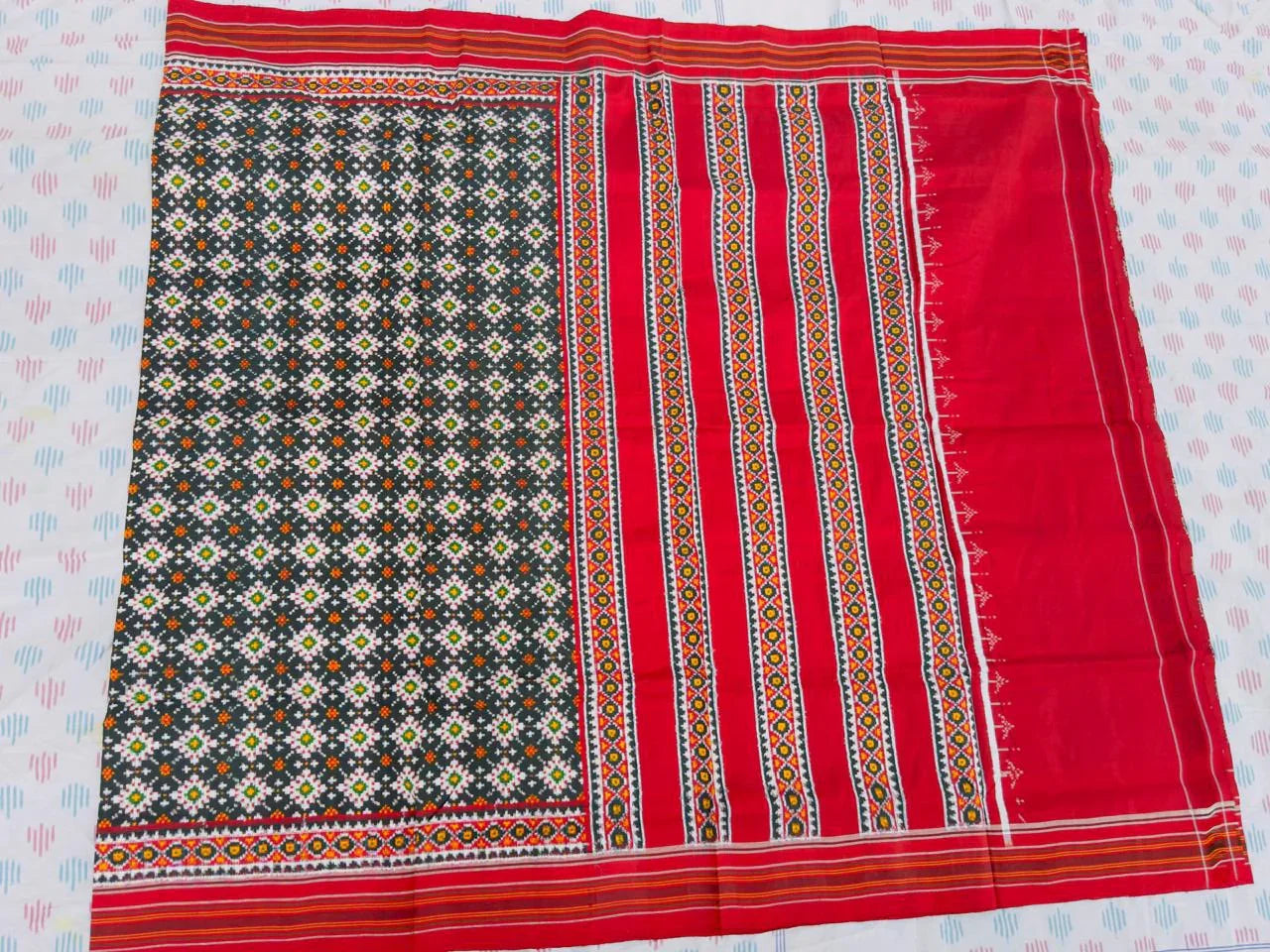 Flat lay of an authentic double ikat patola silk saree with a charcoal black geometric patterned body, red striped pallu, and Silk Mark certification