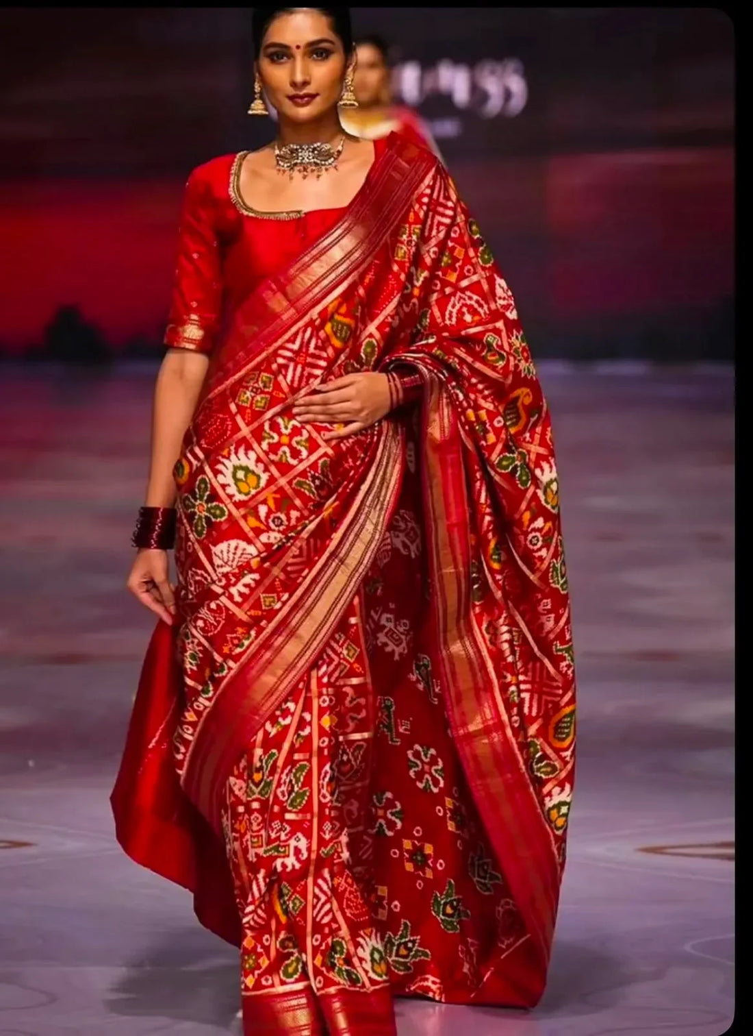 Runway model wearing a luxury crimson red handloom pure silk Patola saree with gold zari border and traditional Ikat patterns.