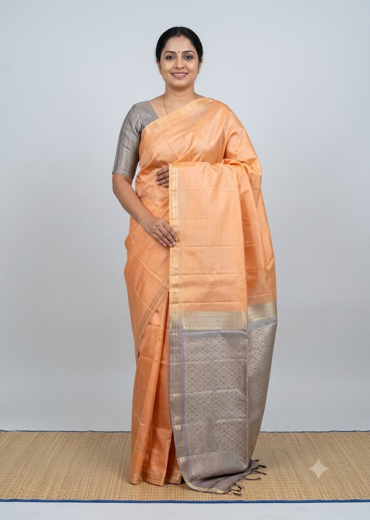 Traditional Indian woman wearing a soft peach Kanchi soft silk saree with a contrast silver-grey zari border and matching grey blouse