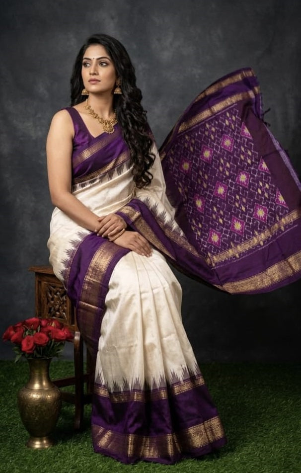 Indian woman seated wearing an elegant off-white ikkat silk saree with a royal purple gold zari border and temple design