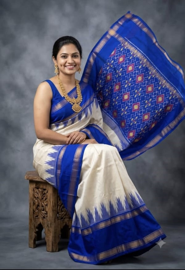 Indian woman seated wearing an elegant off-white ikkat silk saree with a royal purple gold zari border and temple design