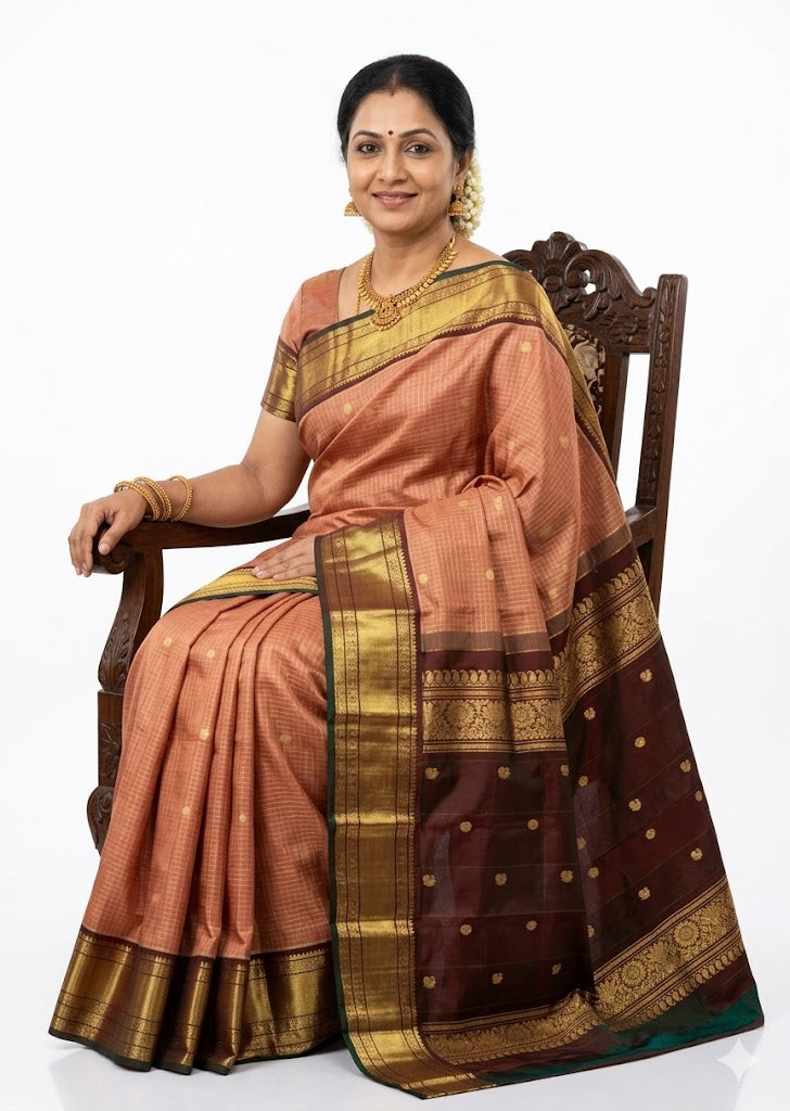 A woman sitting on a wooden chair wearing a traditional Kanchipuram pure silk saree with a peach checkered body and a heavy dark maroon zari border