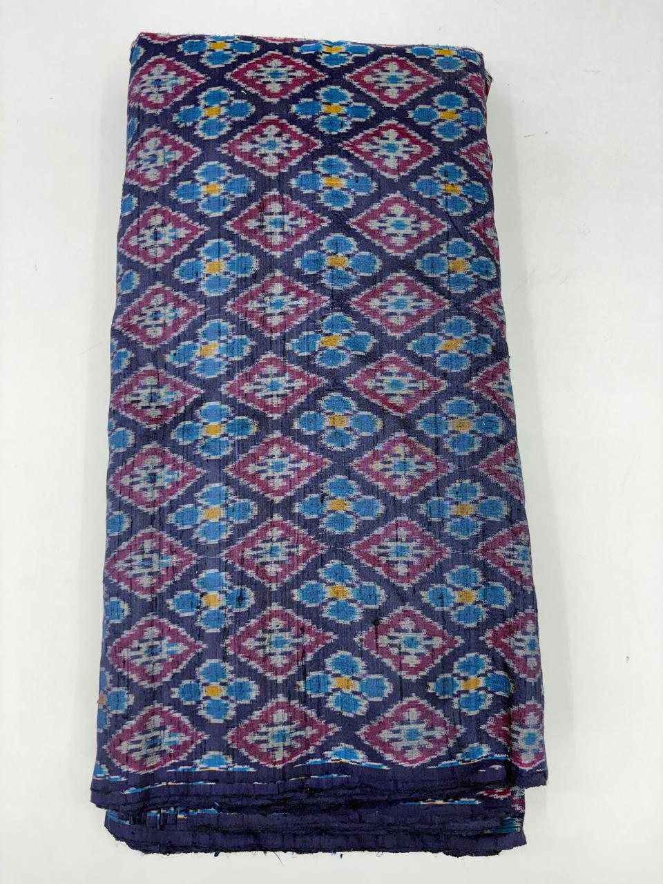 Folded bolt of deep purple pure raw silk fabric featuring multicolored floral and diamond Ikat motifs with Silk Mark quality weave