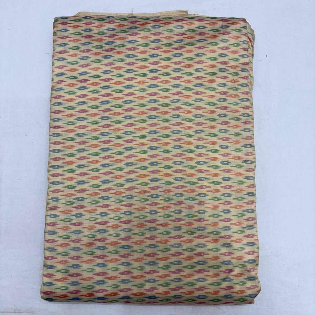 Folded beige cream pure silk Ikat fabric featuring delicate multicolored geometric arrow motifs with Silk Mark certification.