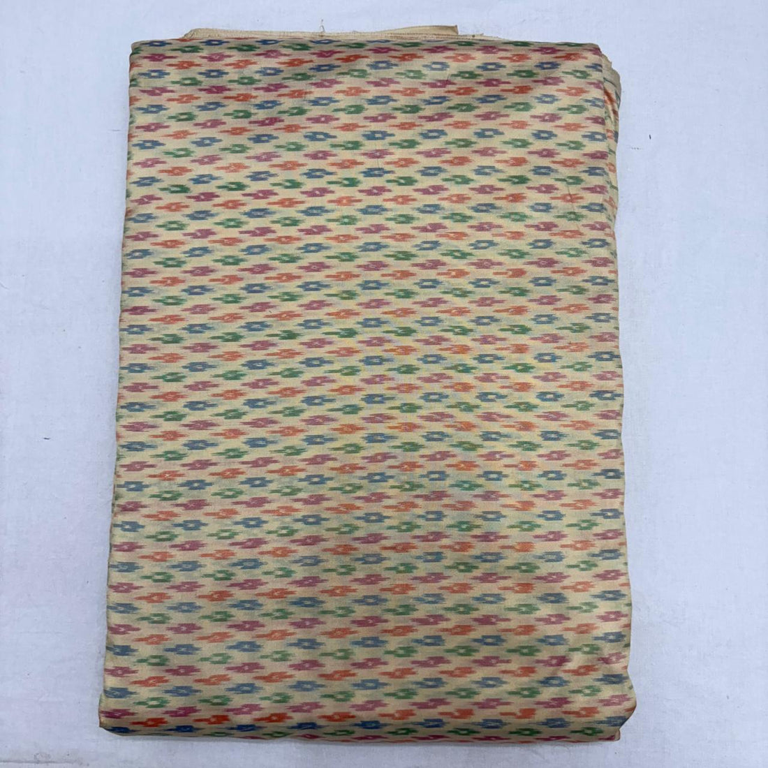 Folded beige cream pure silk Ikat fabric featuring delicate multicolored geometric arrow motifs with Silk Mark certification.