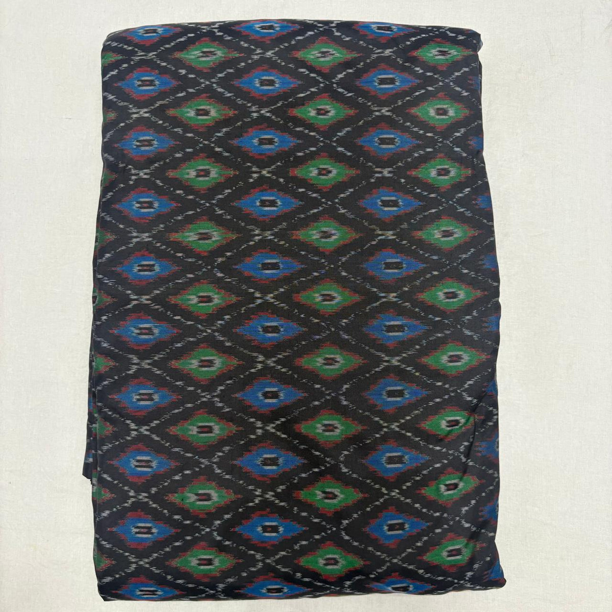 Folded black handwoven pure silk Ikat fabric featuring vibrant royal blue and emerald green geometric diamond patterns with Silk Mark certification.