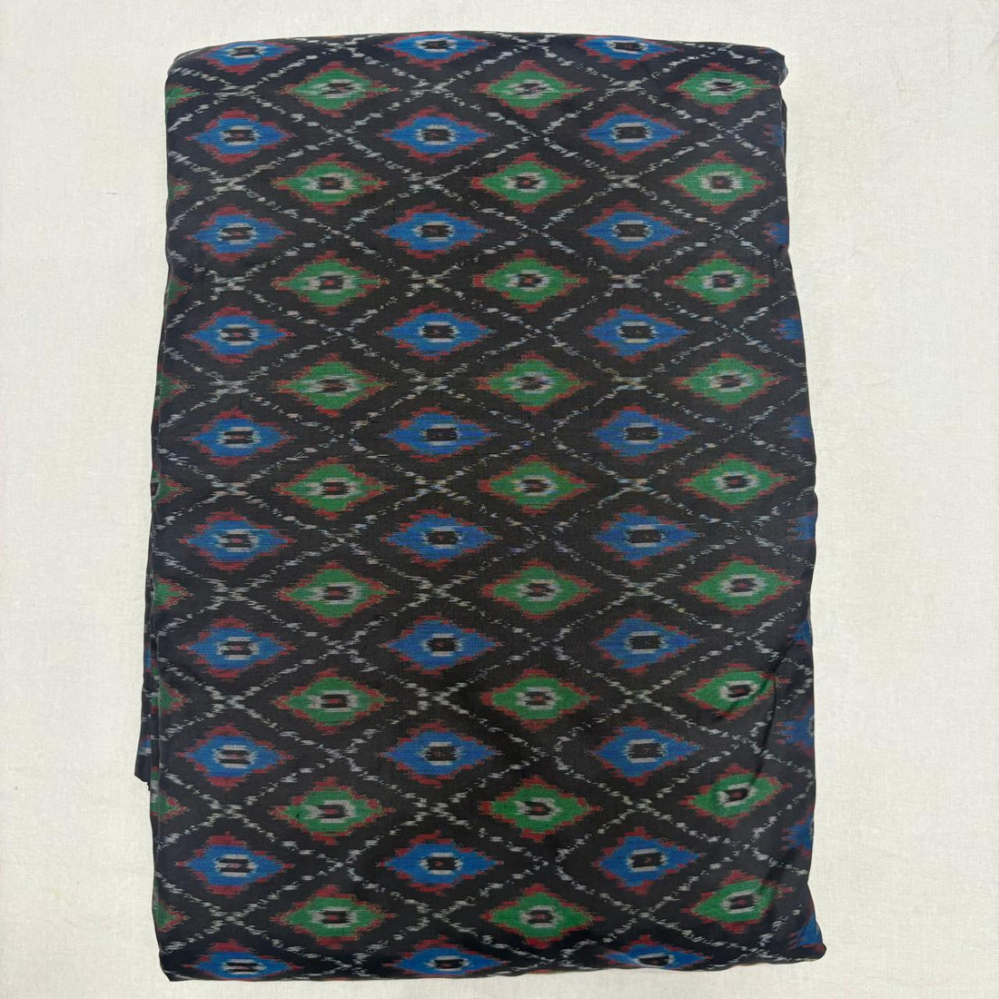 Folded black handwoven pure silk Ikat fabric featuring vibrant royal blue and emerald green geometric diamond patterns with Silk Mark certification.