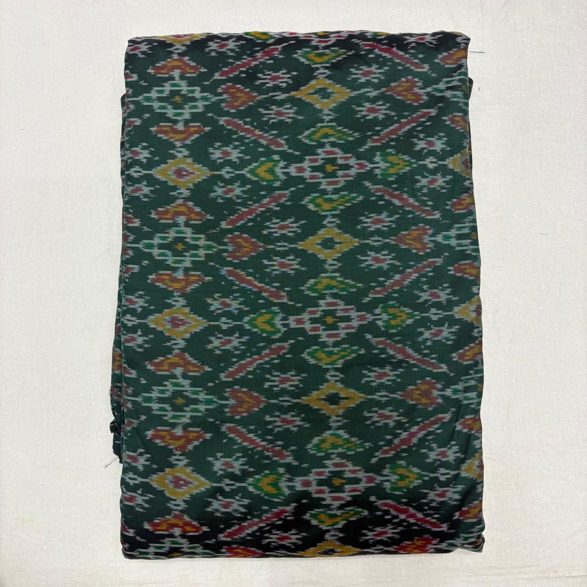 Folded deep forest green pure silk Ikat fabric featuring traditional geometric diamond and rust motifs with Silk Mark certification.