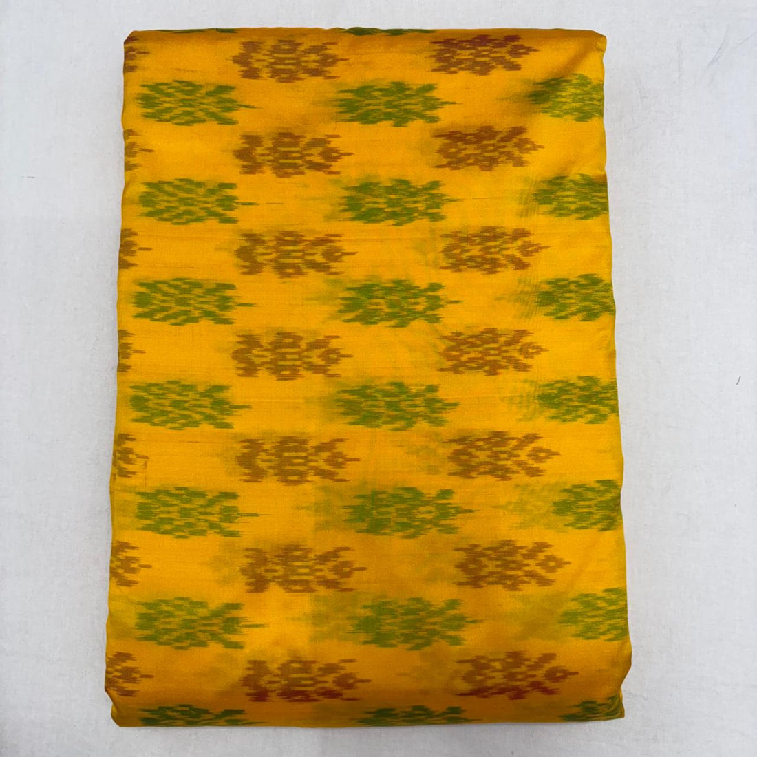 Folded vibrant mustard yellow pure silk Ikat fabric featuring alternating olive green and rust ikat butis with Silk Mark certification