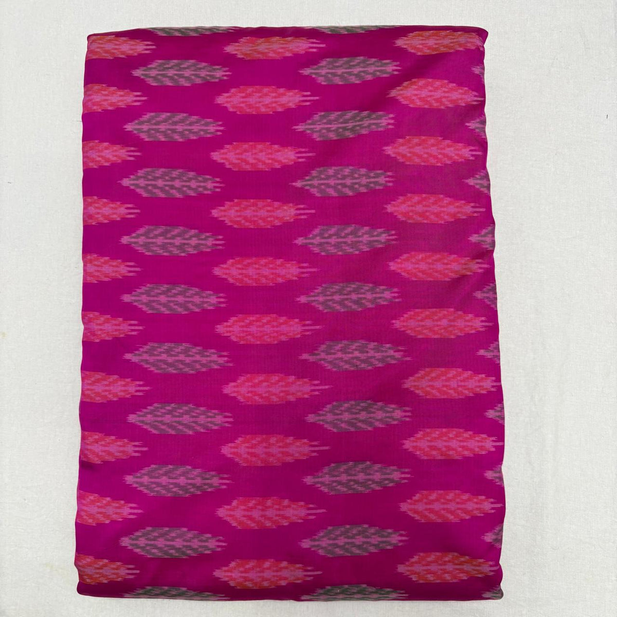 Folded radiant Rani pink pure silk Ikat fabric featuring linear rows of grey and coral leaf motifs with Silk Mark certification