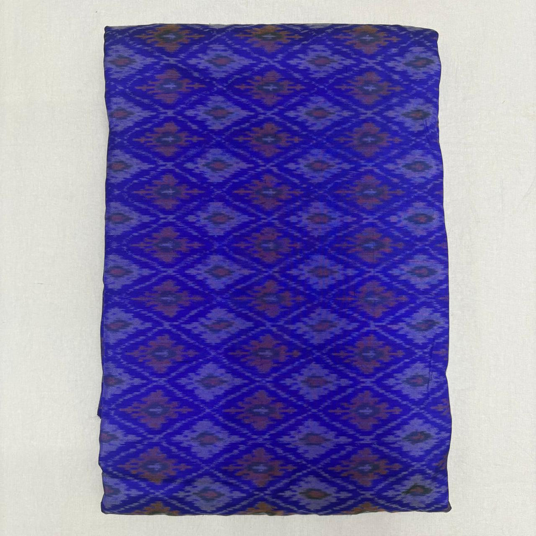 Folded royal blue pure silk Ikat fabric featuring geometric diamond lattice patterns in plum and violet with Silk Mark certification.