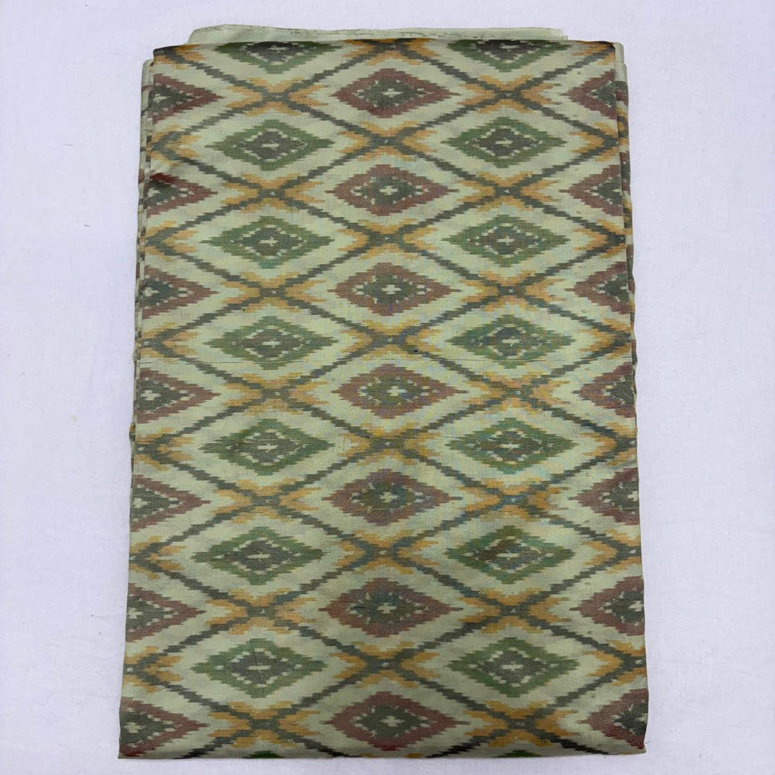 Folded pale sage cream pure silk Ikat fabric featuring olive green, mustard yellow, and rust geometric diamond patterns with Silk Mark certification