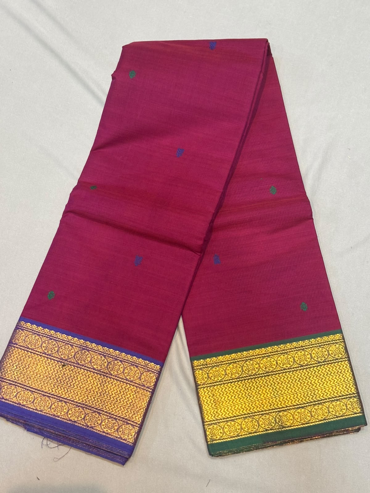 Rani pink Kanchi cotton saree showcasing fine woven buttas and contrasting purple and green gold zari borders with running blouse piece.