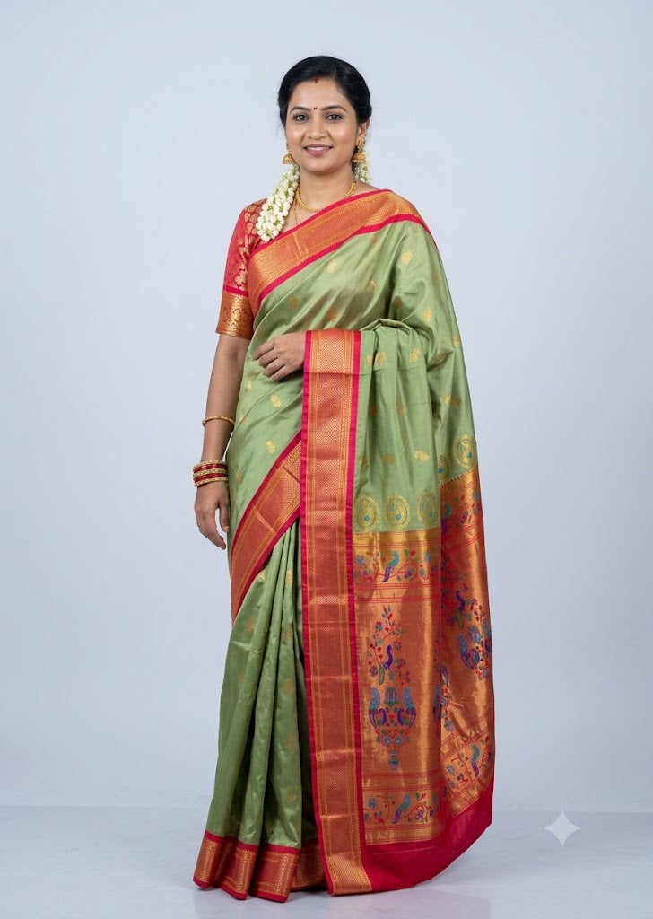 Traditional Indian woman smiling and modeling a light green Semi Gadwal Paithani saree with a rich red and gold peacock motif border, paired with a matching red zari-border blouse, standing against a light gray backdrop.