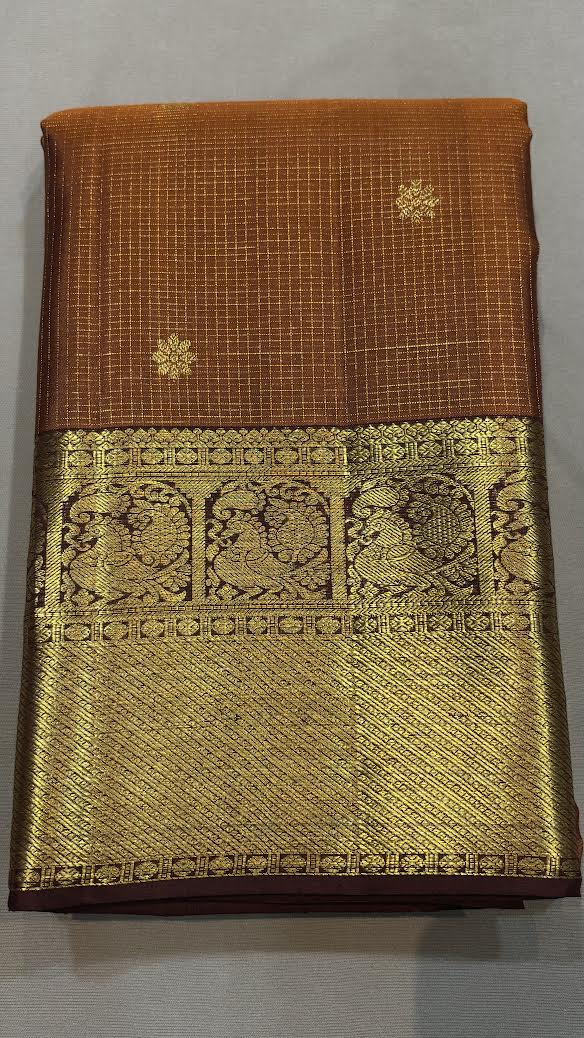 Close-up of a handwoven brown Kanchipuram pattu saree fabric showing intricate floral gold zari butta motifs and a traditional contrast border.