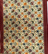 Close-up of cream Patola Ikat fabric featuring a geometric grid with elephant, parrot, and floral motifs, bordered by striped maroon edges.