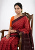 A woman draped in a traditional pure cotton Ikkat handloom saree featuring a bright red body with white geometric patterns and a dark maroon border.