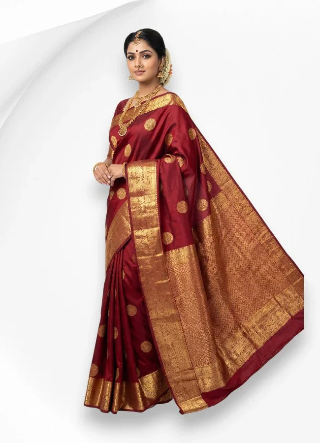 A woman elegantly draped in a traditional deep maroon pure kanchi pattu saree featuring a heavy woven gold zari border, motifs, and matching traditional jewelry.