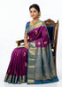 Beautiful woman sitting on a wooden chair wearing a pure purple Kanchipuram pattu saree featuring gold zari motifs and a heavy contrast blue pallu.