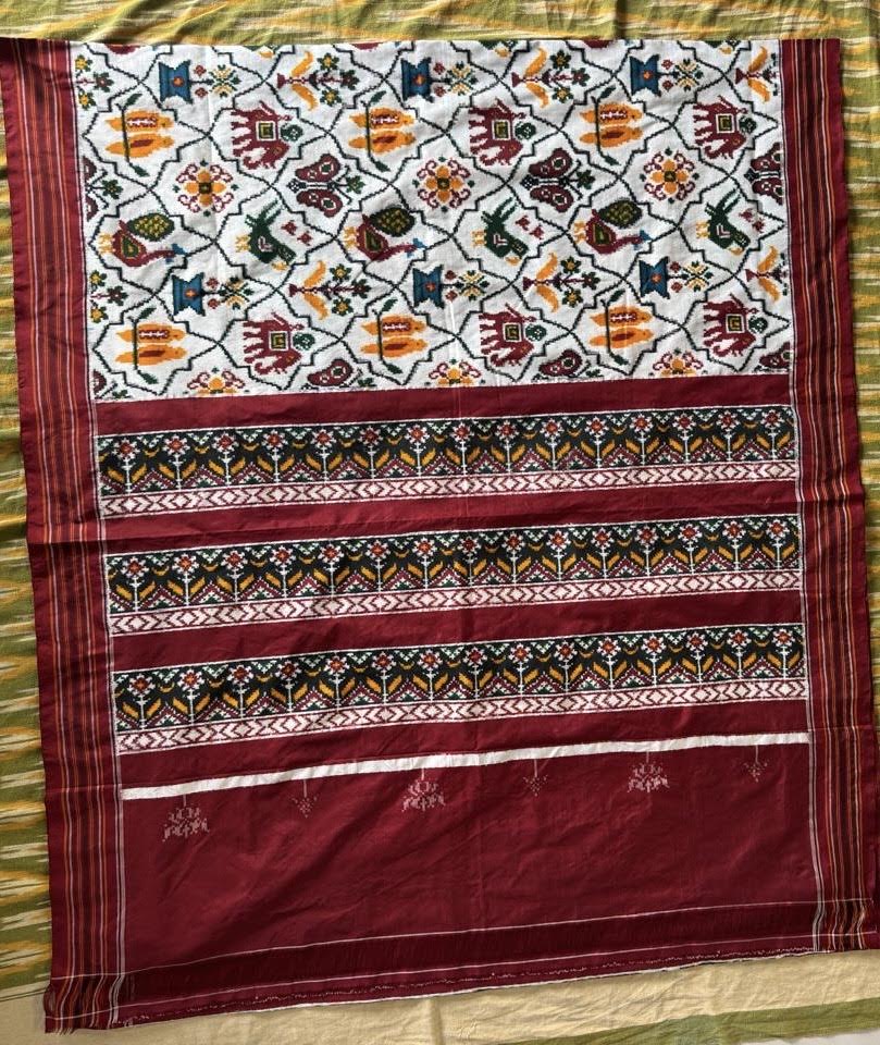 Flat lay of a traditional Patola Ikat saree with a white body featuring elephant and parrot motifs, and a contrasting rich maroon pallu.
