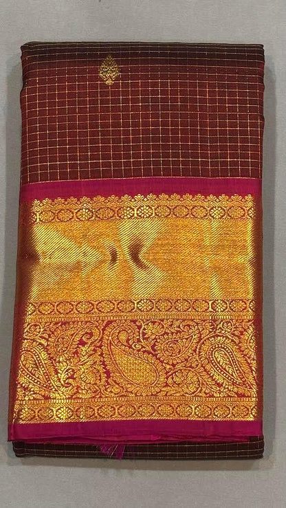 A woman seated elegantly wearing an authentic maroon Kanchipuram pattu saree featuring gold zari micro-checks and a heavy contrasting pink brocade pallu."