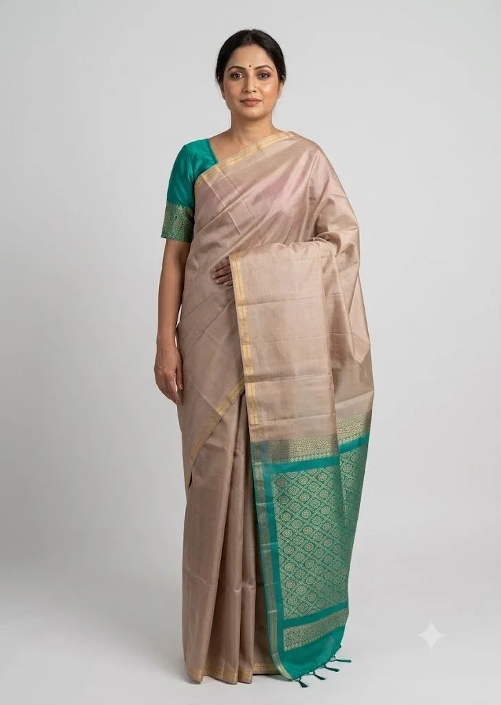 Indian woman wearing a beige silk saree with a teal green zari border and matching blouse against a neutral studio background