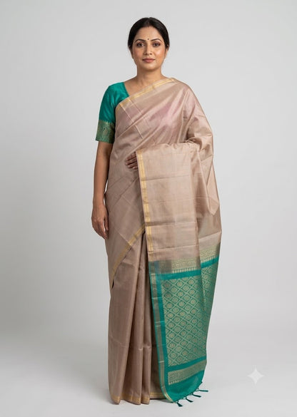 Indian woman wearing a beige silk saree with a teal green zari border and matching blouse against a neutral studio background