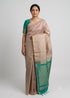 Indian woman wearing a beige silk saree with a teal green zari border and matching blouse against a neutral studio background