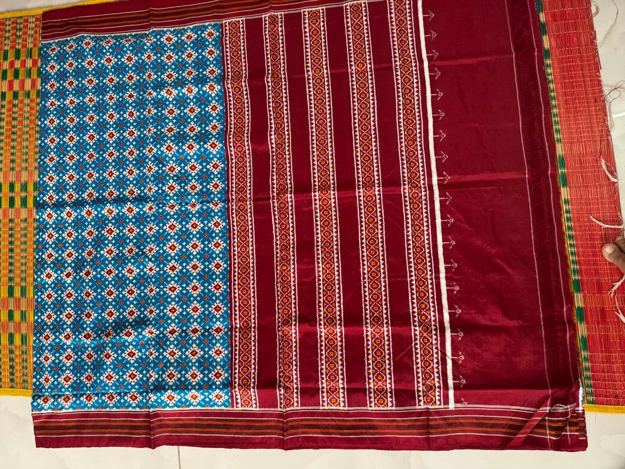 Flat lay of an authentic double ikat patola silk saree with a bright blue geometric patterned body, maroon striped pallu, and Silk Mark certification