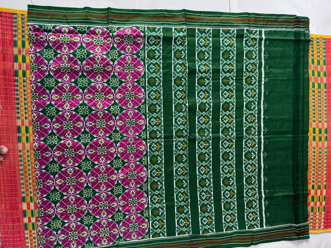 Flat lay of an authentic double ikat patola silk saree with a bold green body, large magenta circular motifs, green striped pallu, and Silk Mark certification