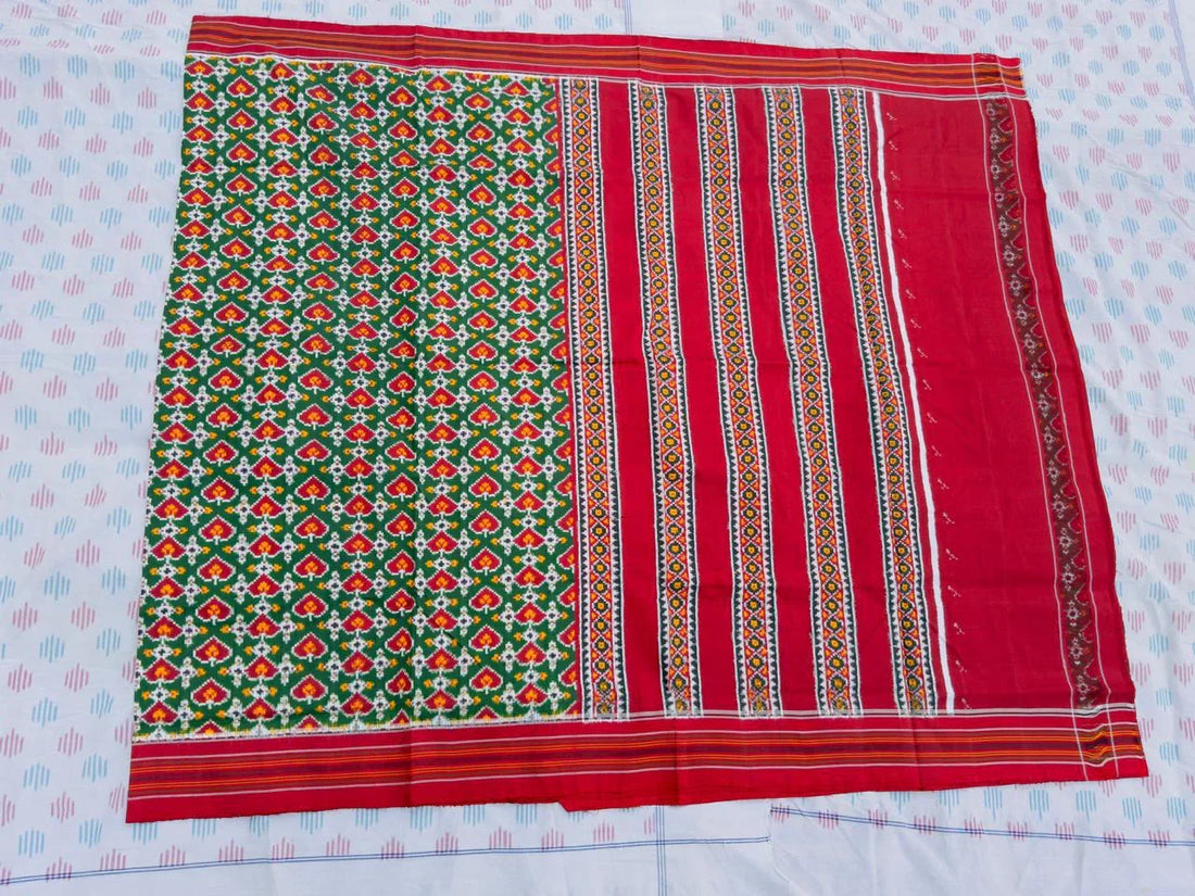 Flat lay of an authentic double ikat patola silk saree with a bold green patterned body, red striped pallu, and Silk Mark certification
