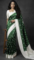 Indian woman standing in an elegant bottle green handloom ikkat silk saree with an off-white border and traditional jewelry