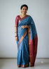 Woman wearing a traditional cerulean blue Kuppadam Pattu saree with wavy silver and copper zari stripes, copper zari border, and contrast wine maroon floral brocade pallu and blouse.