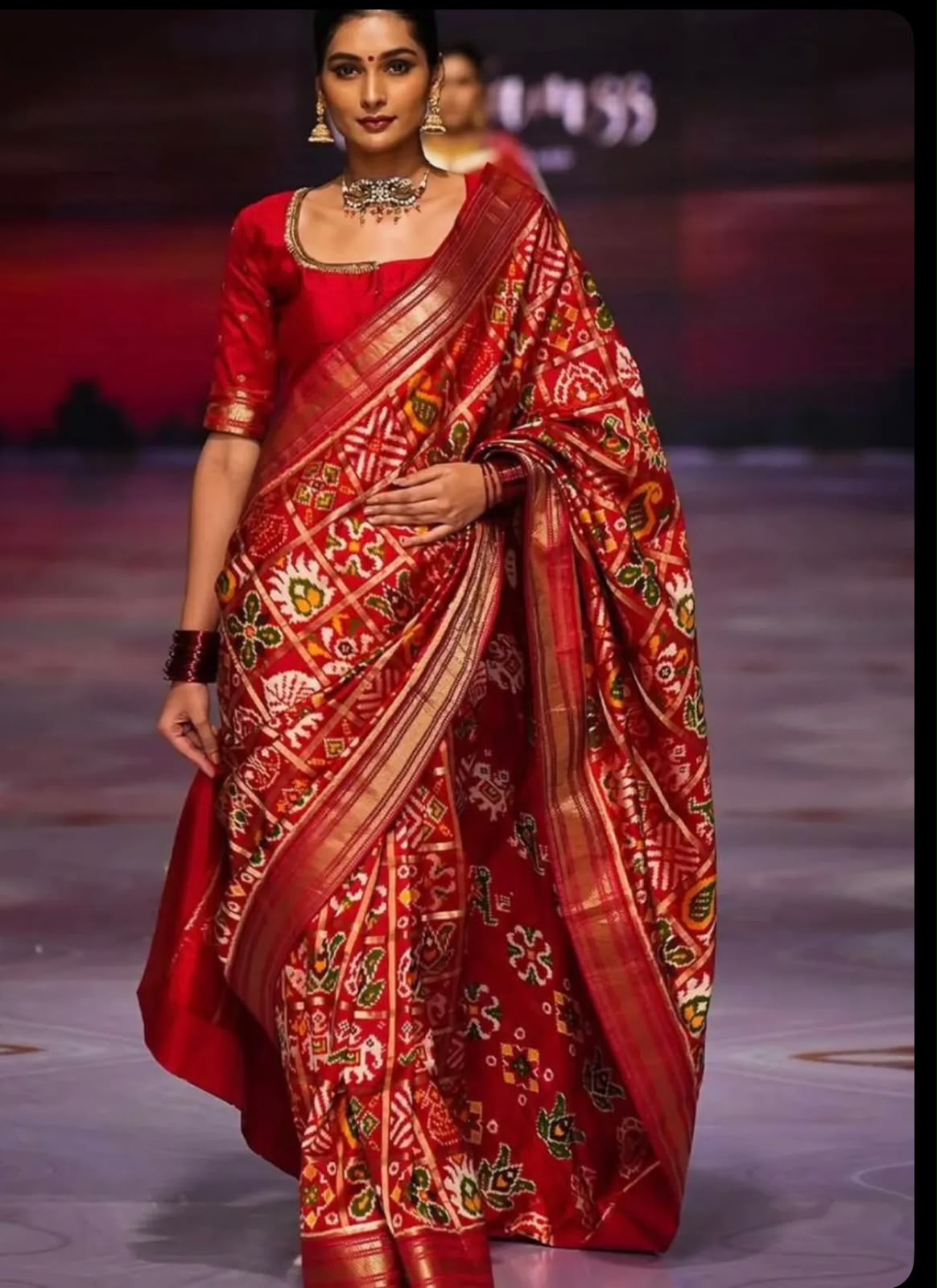 Runway model wearing a luxury crimson red handloom pure silk Patola saree with gold zari border and traditional Ikat patterns.