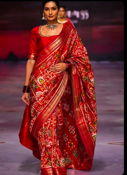 Runway model wearing a luxury crimson red handloom pure silk Patola saree with gold zari border and traditional Ikat patterns.