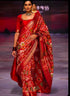 Runway model wearing a luxury crimson red handloom pure silk Patola saree with gold zari border and traditional Ikat patterns.