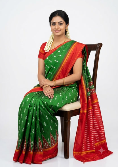 Traditional Indian woman wearing an emerald green and crimson red Pochampally Ikat pure silk saree seated on a wooden chair against a white background