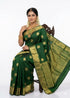 A smiling South Indian woman seated gracefully, draped in a traditional emerald green pure kanchi pattu saree featuring gold zari coin motifs and a grand heavy border, styled with classic temple jewelry.