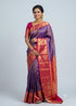 A traditional South Indian woman posing in a vibrant violet Dharmavaram silk saree with a contrasting pink and gold zari border, pallu, and matching pink blouse against a studio backdrop