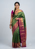 A traditional Indian woman posing in a vibrant green Dharmavaram silk saree with a contrasting magenta and gold zari border, pallu, and matching magenta blouse against a studio backdrop