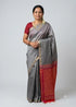 Traditional Indian woman wearing a grey silk saree with a crimson red blouse and golden zari pallu against a neutral grey background