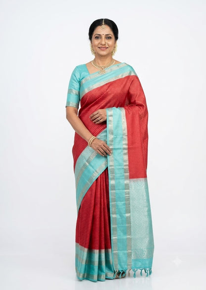 Elegant woman standing draped in a red Kanchi soft silk checks saree with a teal blue silver zari border against a plain white background