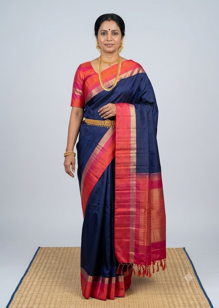 Traditional Indian woman wearing a navy blue Kanchi soft silk saree with a pink and orange gold zari border and matching blouse
