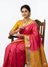 Traditional Indian woman seated on a wooden chair wearing a pink Kanchi soft silk saree with a mustard yellow border and matching blouse, isolated on a white background.