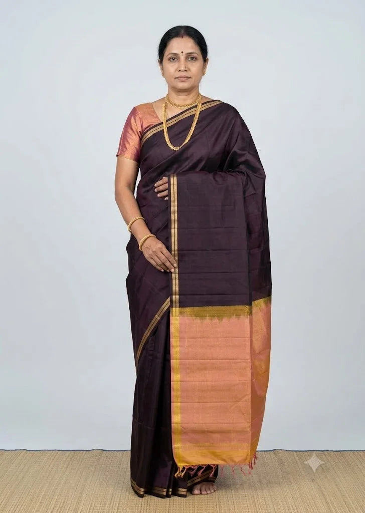 Traditional Indian woman posing in a deep wine-black Kanchi soft silk saree featuring a peach-gold zari border and matching peach blouse